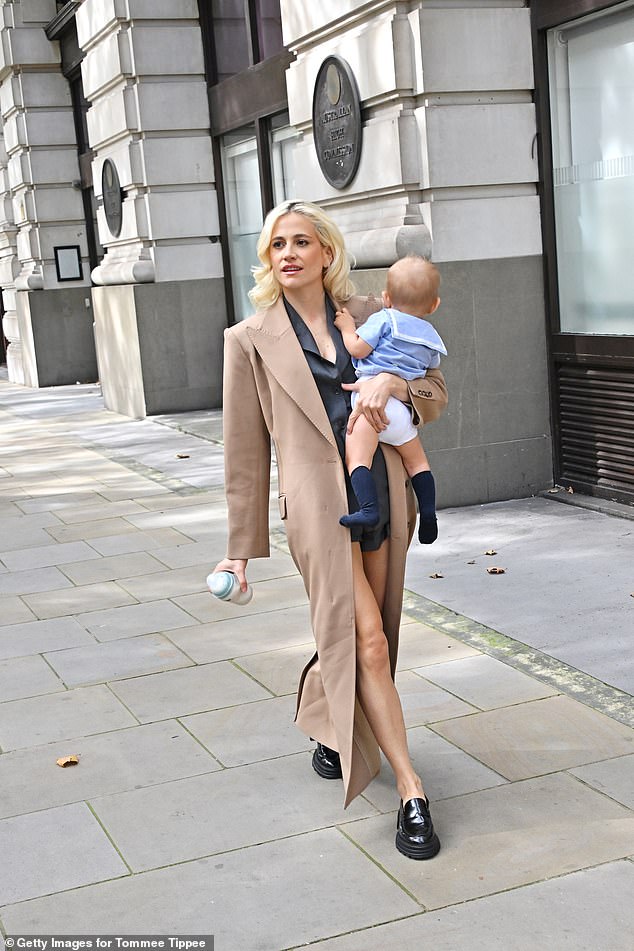 Sporting her usual peroxide blonde locks, the new mother wore a floor-length camel overcoat over a short trouser suit