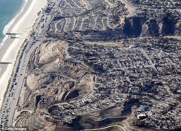 An aerial view of fire trucks, utility, and other vehicles parked along Pacific Coast Highway near homes destroyed in the Palisades Fire on Monday