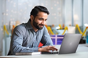 Man working on his Dell laptop in an office. He is smiling as he works.