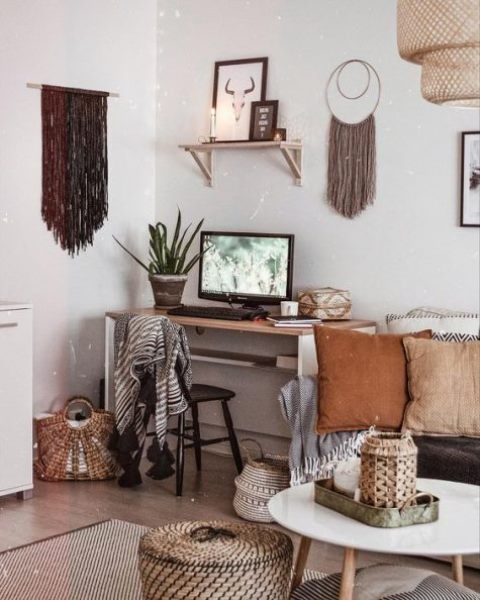 A boho home office with long fringe hanging, a sleek desk, lots of basket for storage and earthy tone pillows.