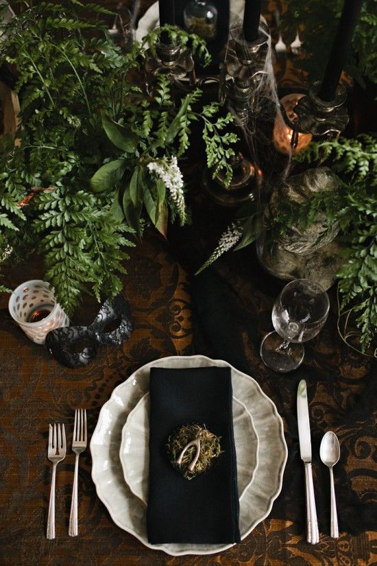 A vintage Halloween table setting with black and white touches, greenery, black candles in vintage candleholders, spiderwebs and hay is a creative idea.