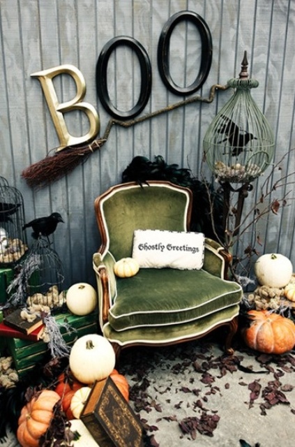 A vintage Halloween nook with a green vintage chair, stacks of vintage books, pumpkins, a broom and some letters.