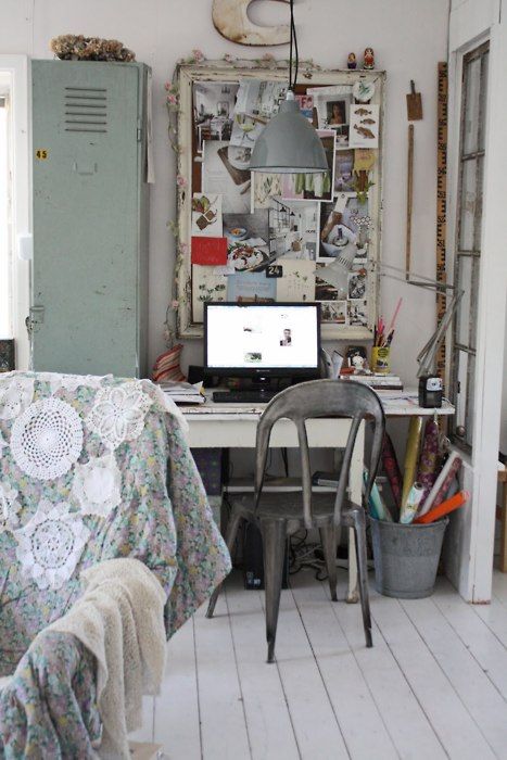 A boho chic and shabby home office with white walls and floor, a green storage unit, a memo board with various photos and ideas, a metal chair.