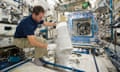 An astronaut in trousers and short-sleeved shirt inserts blood samples into a small freezer onboard the ISS