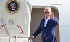 white man wearing blue suit and standing at plane entrance waves