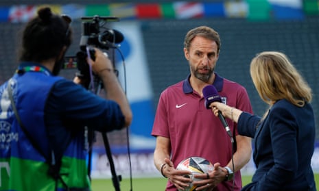 Camera pointed at Gareth Southgate doing  TV interview by the pitch while woman holds microphone to him