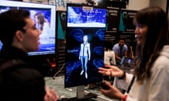 person wearing white talks to person wearing black in front of a screen with image of a person standing