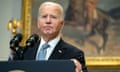 A man standing at a podium wearing a black suit looks off to the side