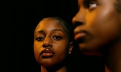 Richly colored image. On the left and right, two Black teenage girls, both wearing orange.