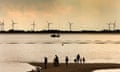 People stand on a beach at Mersea Island in Essex, with views of wind turbines in the background.