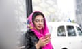 Woman waiting at bus stop, using smartphone.