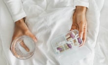 The hands of a woman holding a glass of water and a tray of vitamins