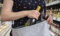 Stock picture of a woman in a supermarket slipping a bottle of wine into her bag