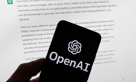 OpenAI logo on a phone in front of a computer screen displaying text