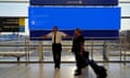 United Airlines staff wait in front of a departures monitor displaying a blue error screen at Newark international airport