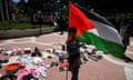 shoes and children's clothes on the ground alongside a child holding a large Palestinian flag