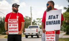 Two people wearing red T-shirts hold signs that read 'honk if you support workers' and 'AT&T unfair'