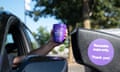 A person driving in a car holds a purple cup reading 'Sip, Return, Repeat' as they prepare to drop it into a receptacle reading 'Reusable cups only'