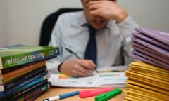 A frustrated male teacher rests his head in his hand as he works his way through piles of marking