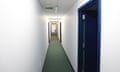 A narrow, windowless corridor with white walls and blue doors and doorframes.