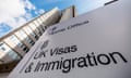 Photo looking up at a sign reading "Home Office: UK Visas & Immigration" with a skyscraper against a cloudy sky behind it