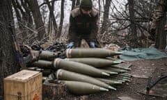 A Ukrainian serviceman crouches over a stack of 155mm artillery shells near Bakhmut in March 2023