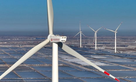 Four wind turbines stand above an array of solar panels covering the ground