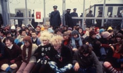 Female protesters seated in front of fence where police several police stand