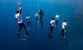 A freediver ascends alongside a rope surrounded by six safety divers