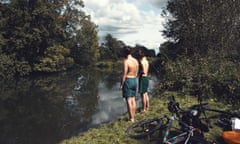 Two boys in swimming trunks stand by the river's edge