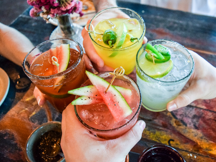 Friends toasting, saying cheers holding tropical blended fruit margaritas. Watermelon and passionfruit drinks. - Image