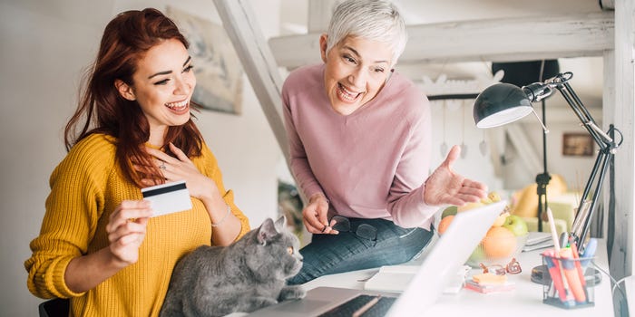 A photo of a young woman and and older woman shopping online with a cat present on the desktop.