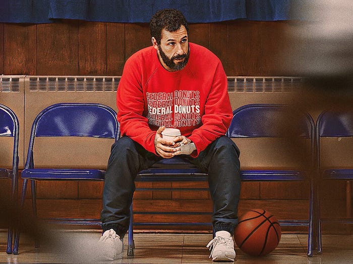 Adam Sandler sitting holding a coffee cup