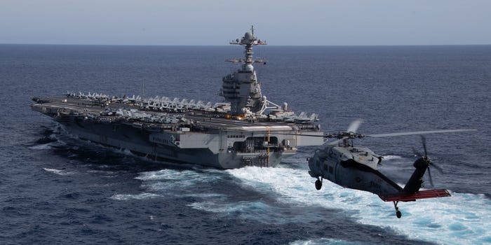 A helicopter approaching an aircraft carrier at sea.