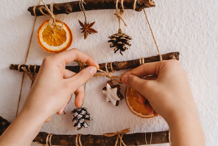 Woman hands decorating handmade craft Christmas tree made from sticks and natural materials hanging on wall. Sustainable Christmas, zero waste, plastic free, eco friendly