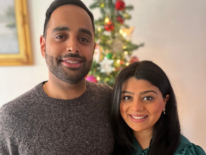 Poojah Shah in a green silk shirt stands next to husband with Christmas tree in background