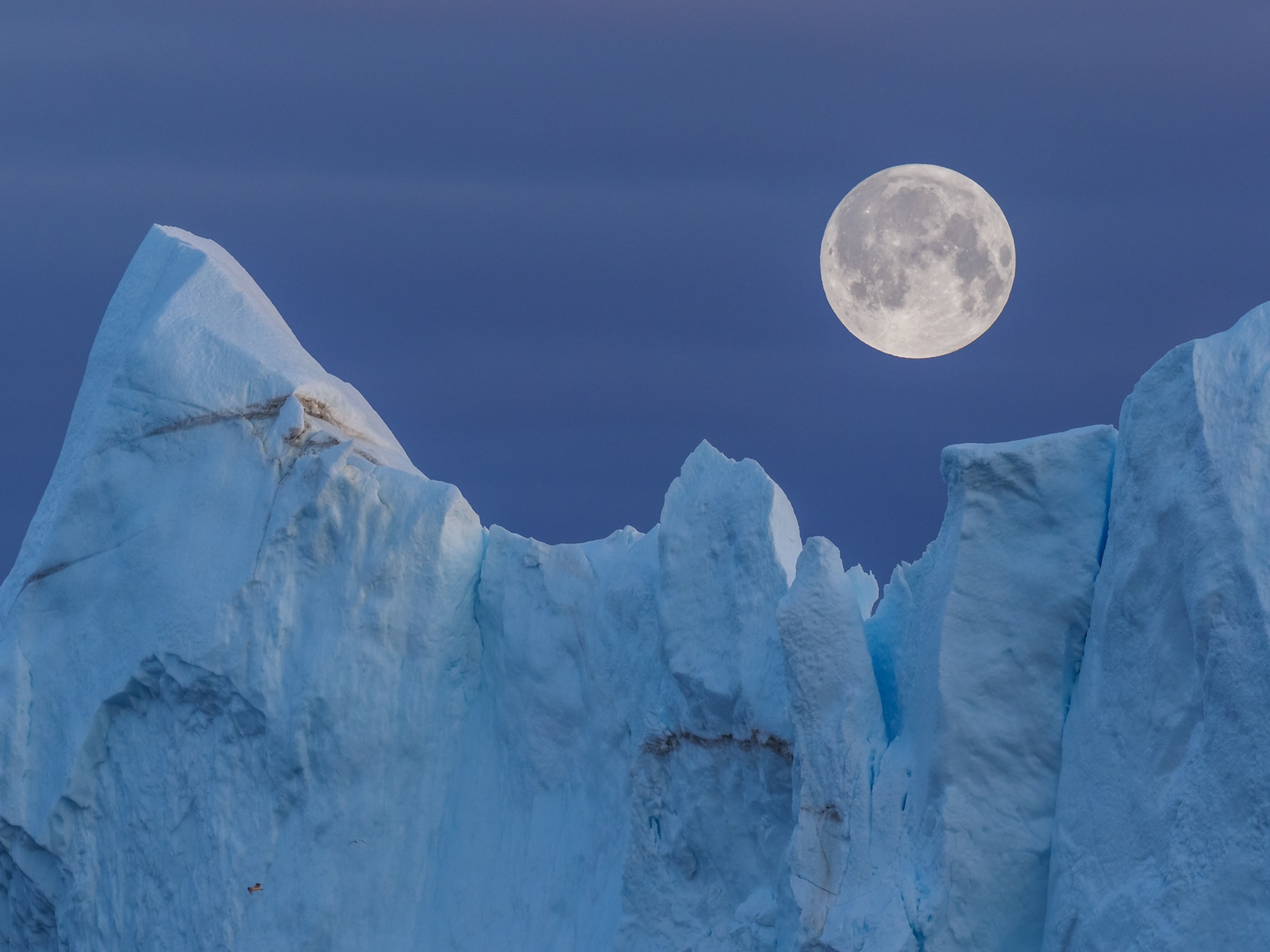 A full moon above the peaks of an iceberg.