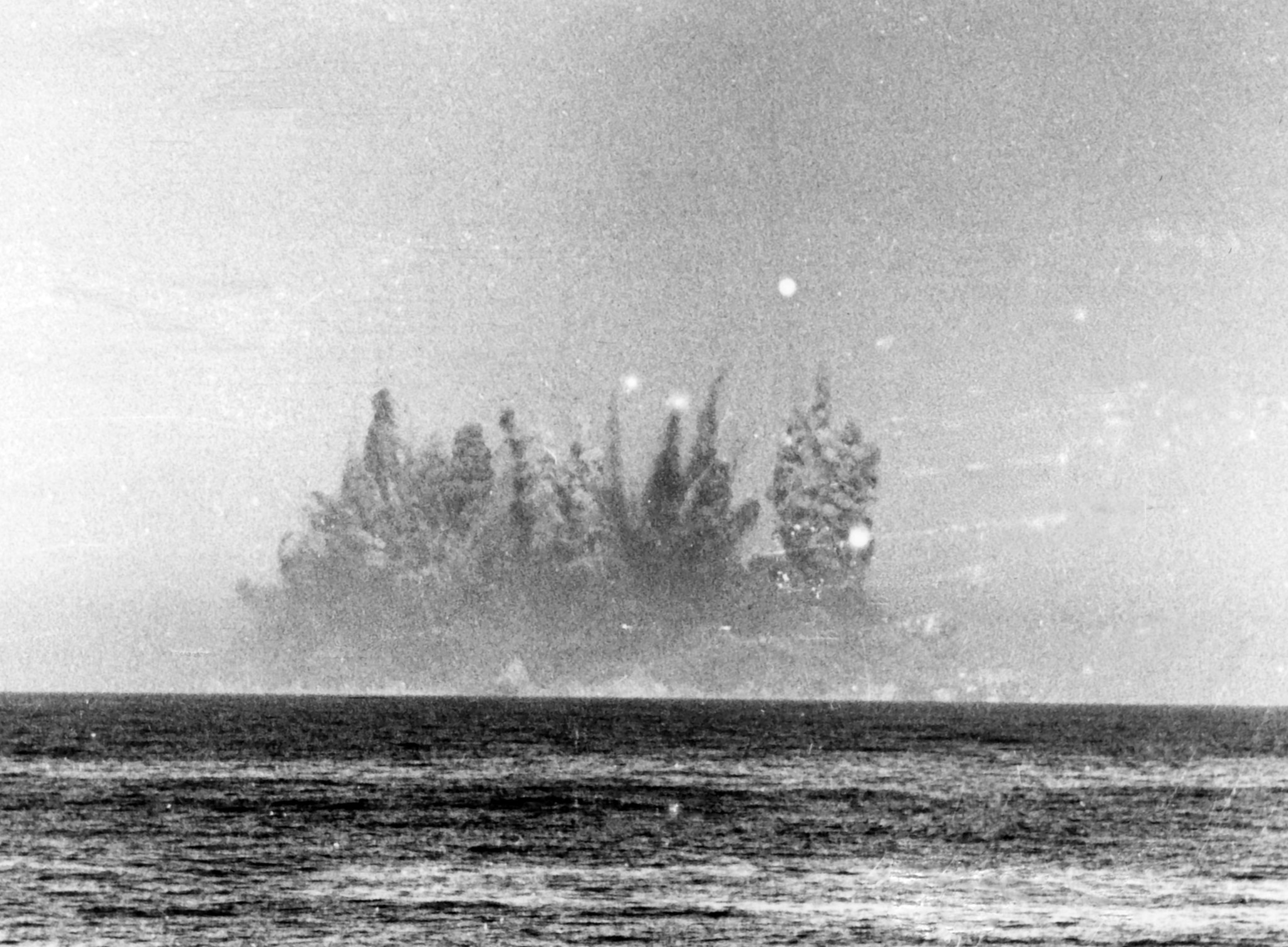 An old black and white photo of a large cloud of smoke and debris rising up from the middle of the sea.