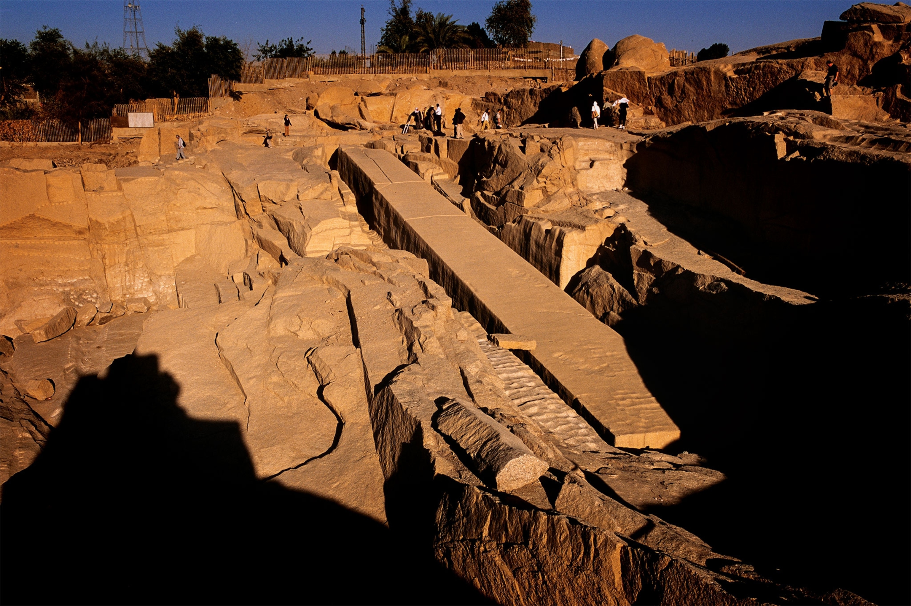 An unfinished, cracked obelisk lies in the ground