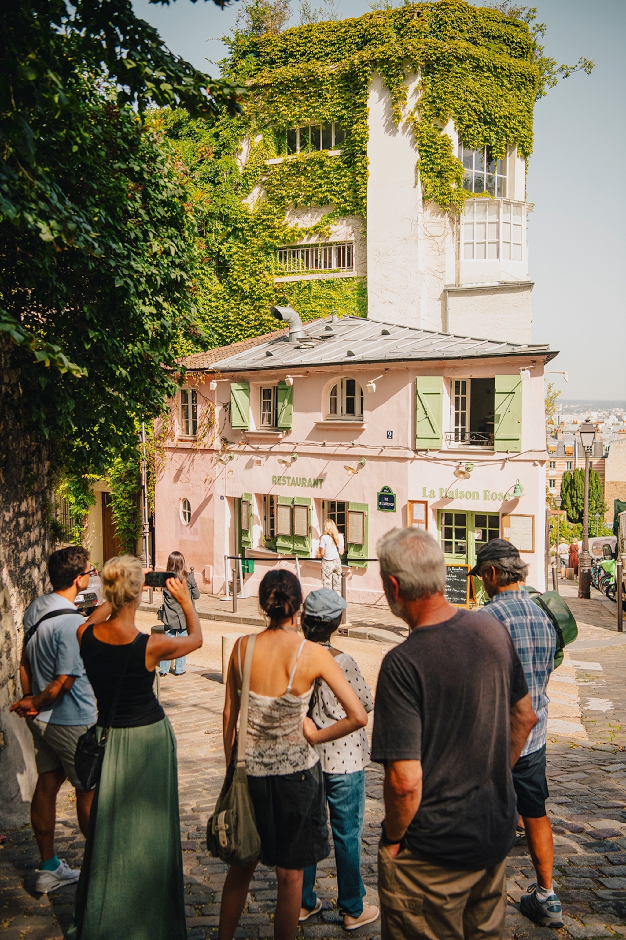 Travellers pausing for photos outside the pink building of La Maison Rose restaurant in Montmartre, Paris.