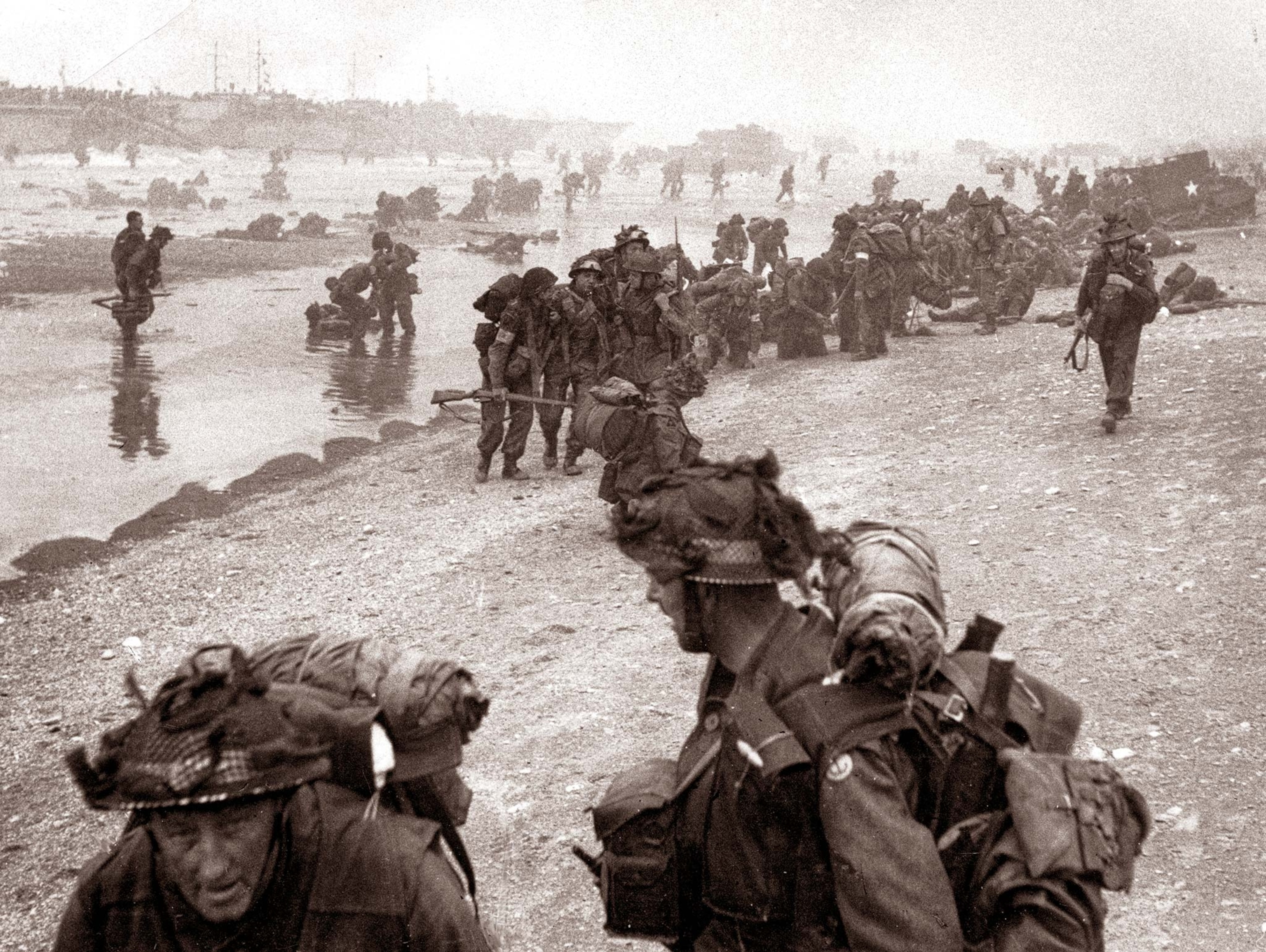 Troops line up on Sword Beach on D-Day, with medics assisting the wounded