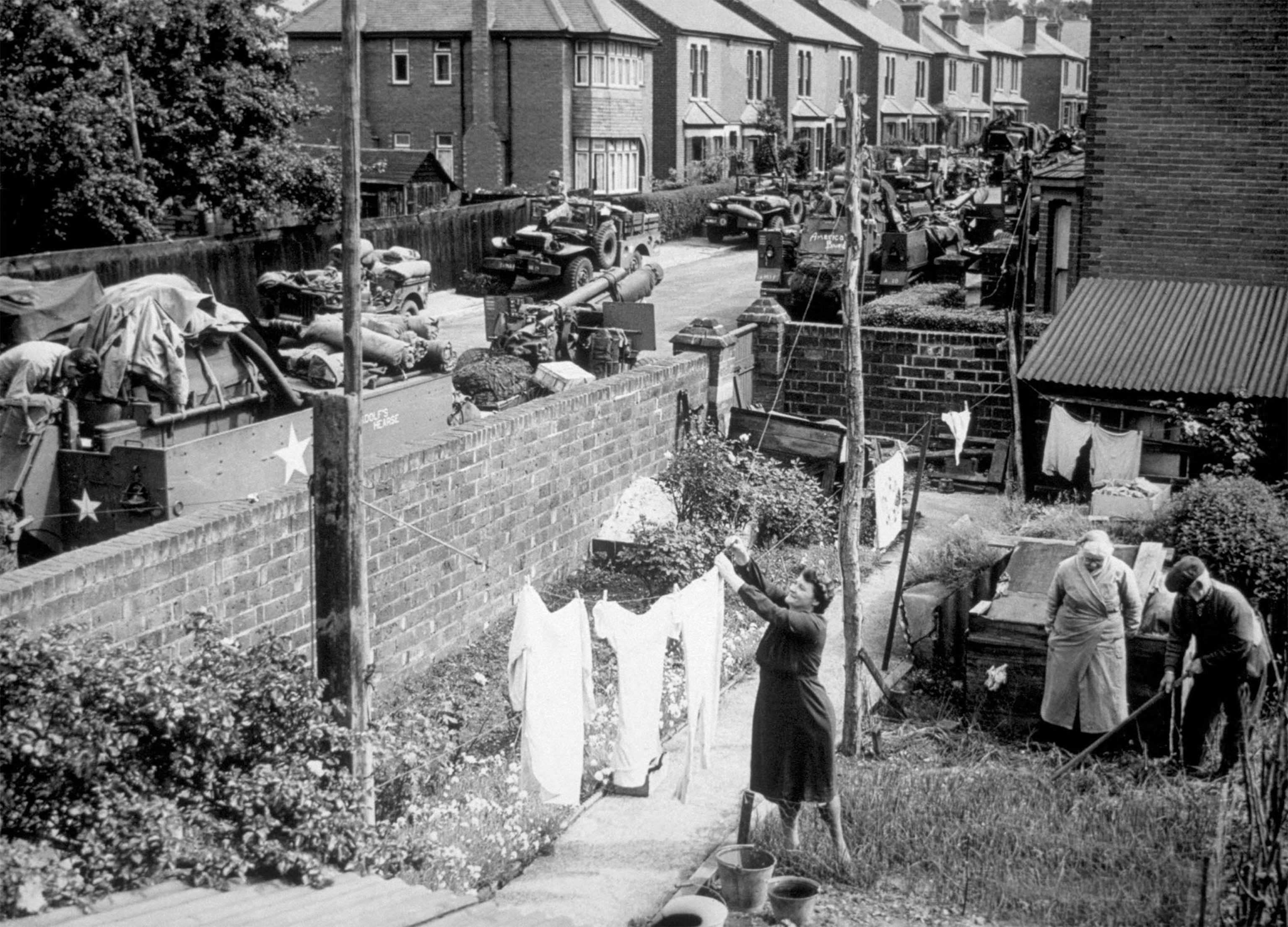 U.S. military vehicles line a Southampton street and await transport to Normandy while Annie Bagg hangs out her wash, as usual, in 1944.