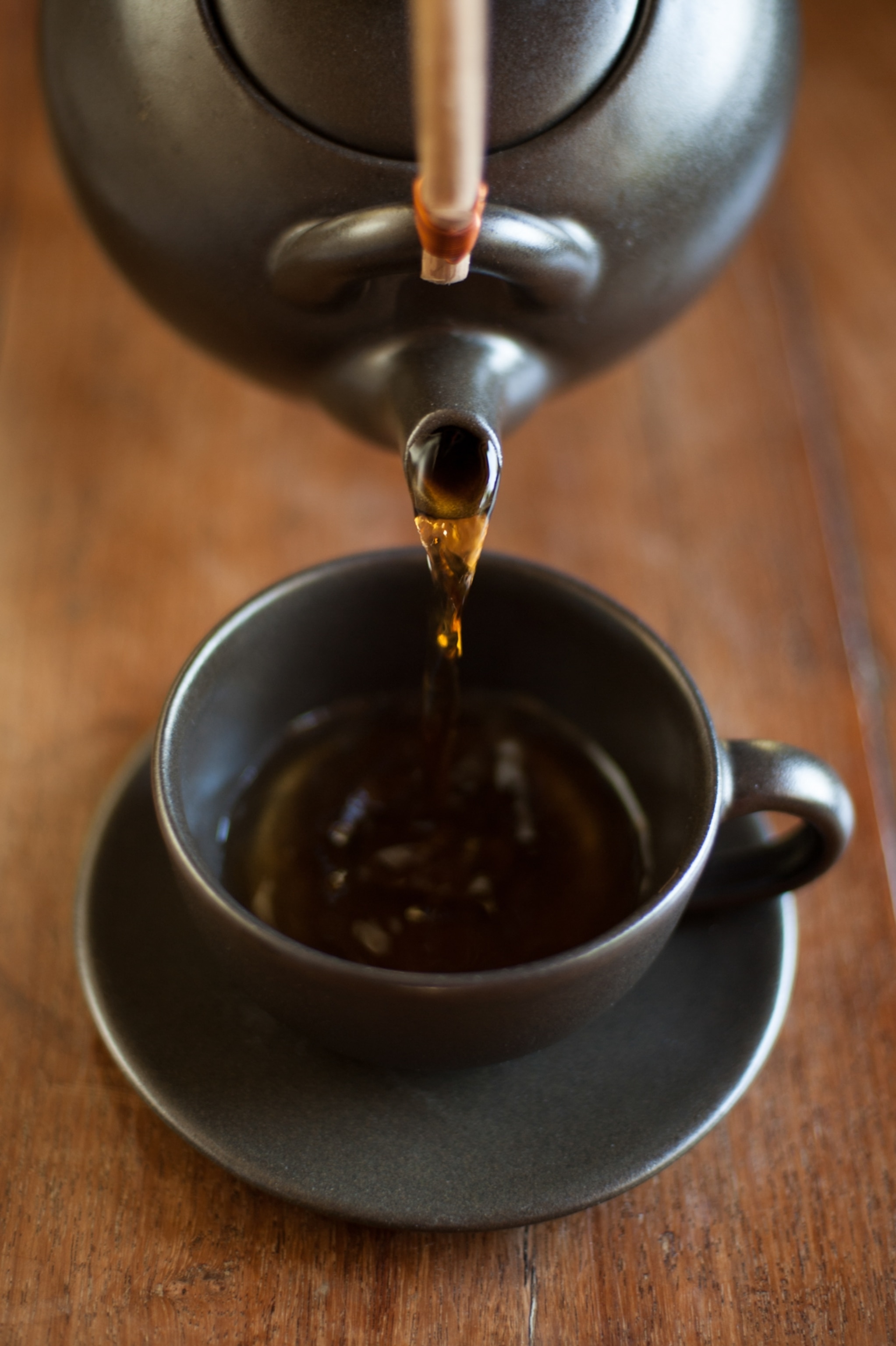 A close up view of tea pouring from a black tea pot into a black teacup.