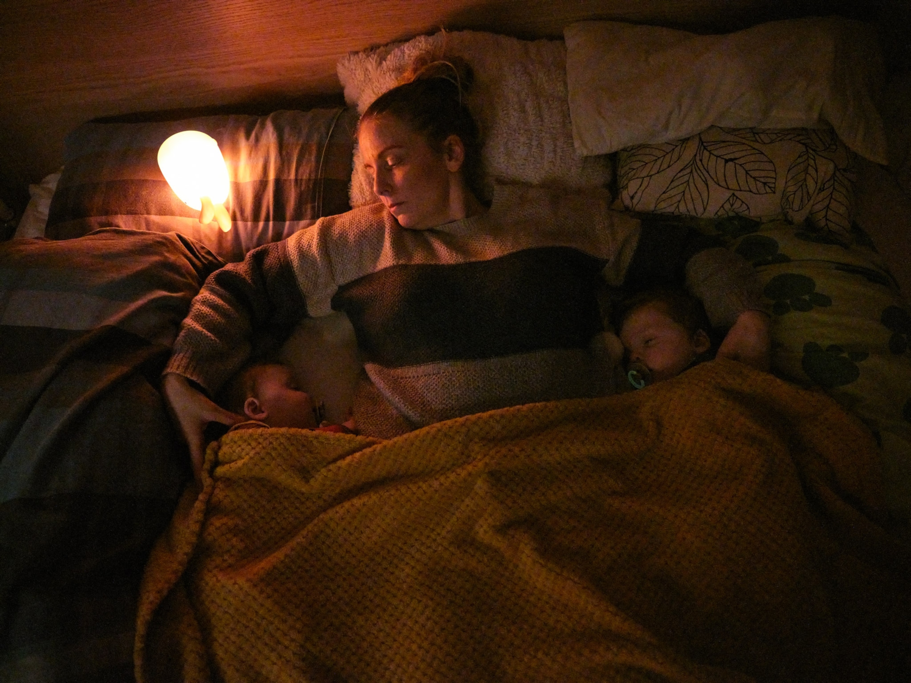 A mother lays down with her infant twins for a nap.