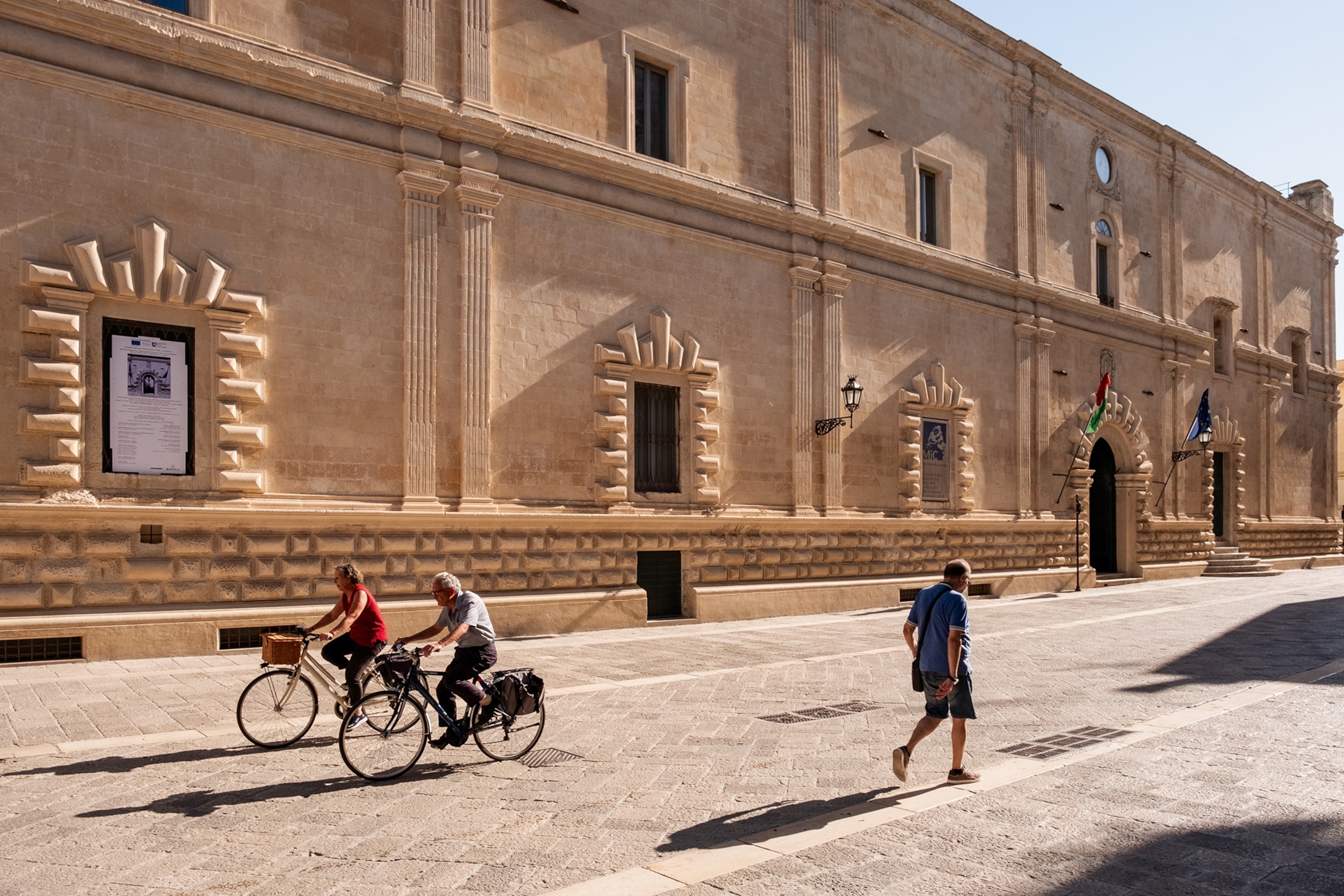 People cycling and walking in front of a sandy coloured stone building