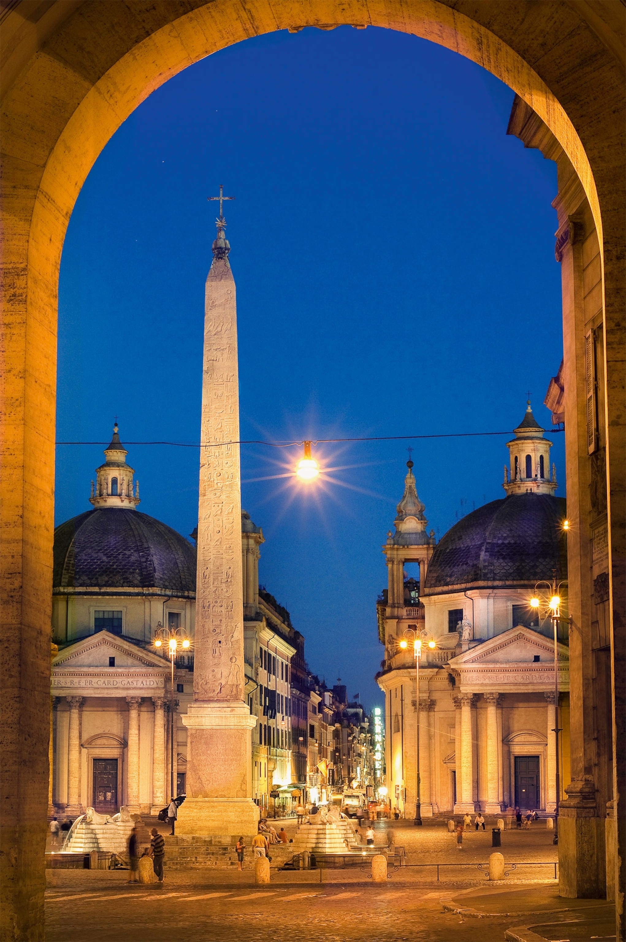 A nighttime view of an obelisk through an archway in Rome