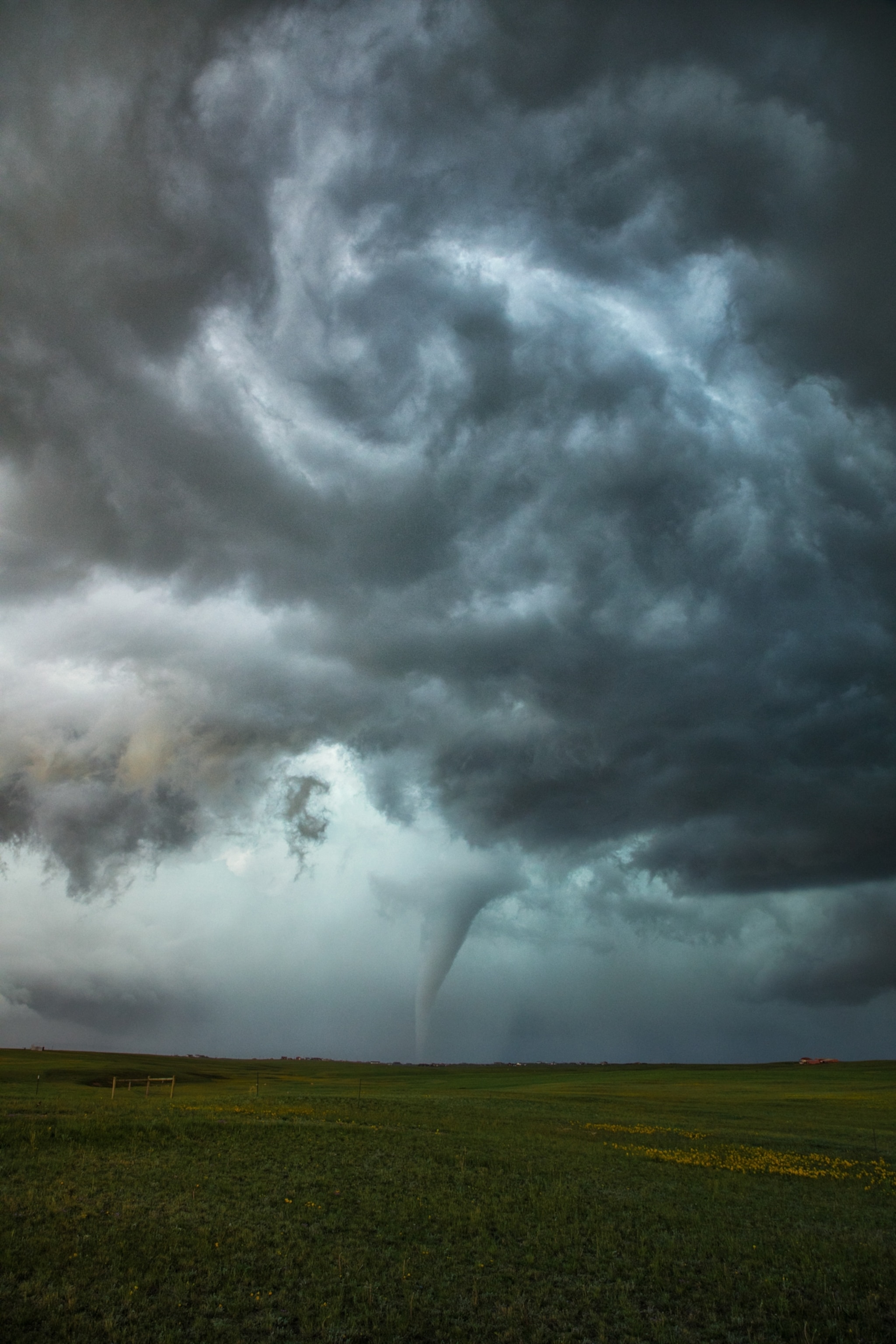 A tornado touching down in grasslands as a massive glowing supercell swirls above