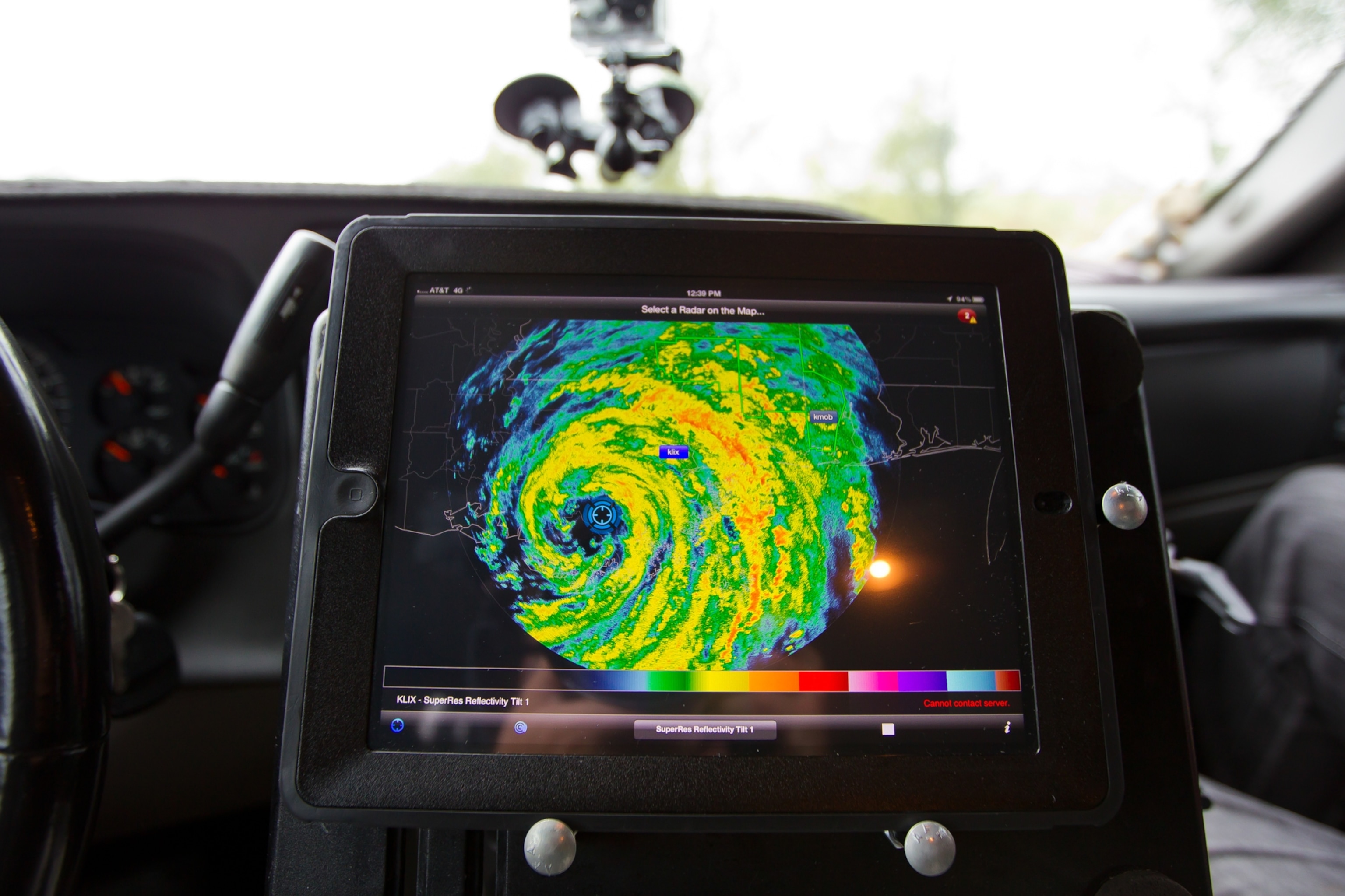 A radar mounted between the front seats of a storm chaser vehicle, which shows a marker indicating the team's location within the eye of a hurricane, visualized by radar as swirls of blue, green, yellow and red depending on the strength of the storm.