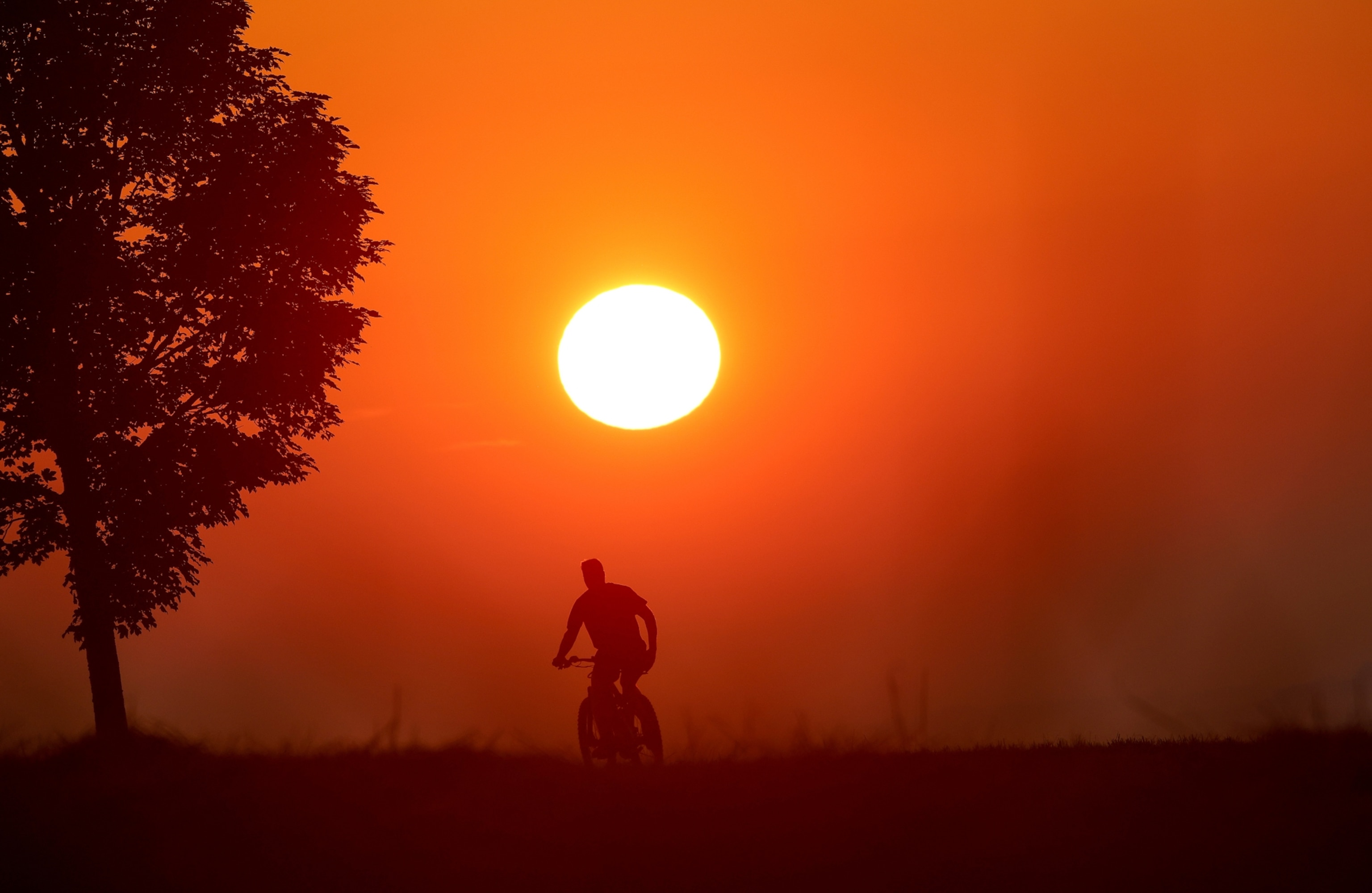 A bicyclist silhouetted against an orange sky at sunrise.