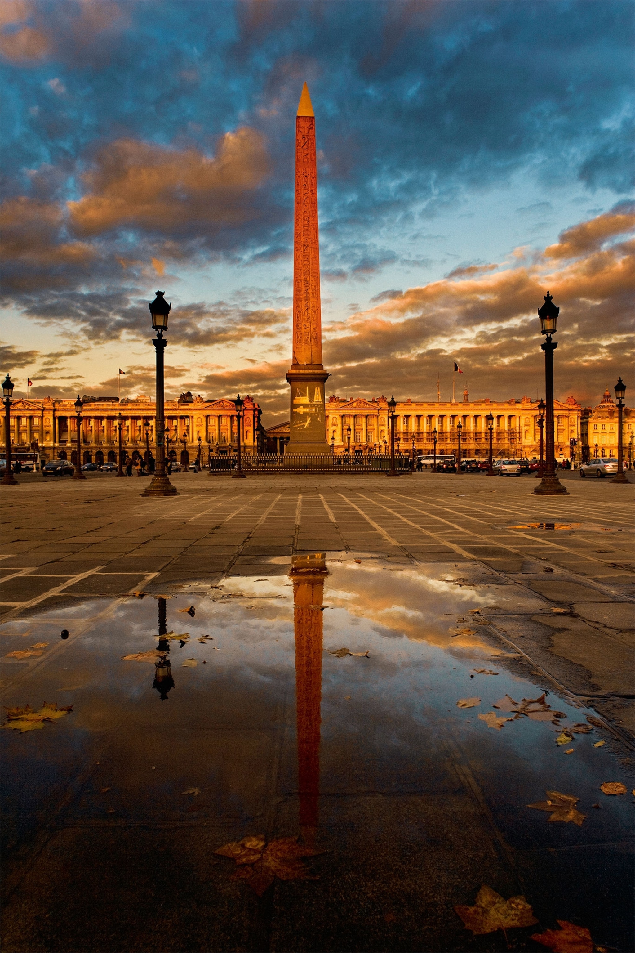 An obelisk towers in a Paris square with its reflection in a puddle